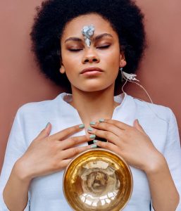 woman lying on her back with petals on her forehead and a bowl on her stomach.